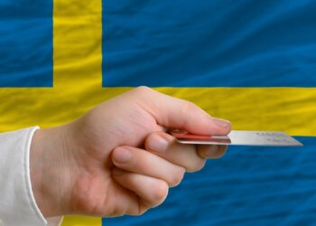 A hand holding a credit card and Sweden's flag is in the background.