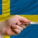 A hand holding a credit card and Sweden's flag is in the background.
